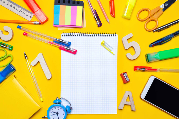 school accessories on a desk on a yellow background. concept of education. stationery. watches, colored pens, phone, markers. notebook. view from above. copy space. top view. flat lay. copy space - Photo, image