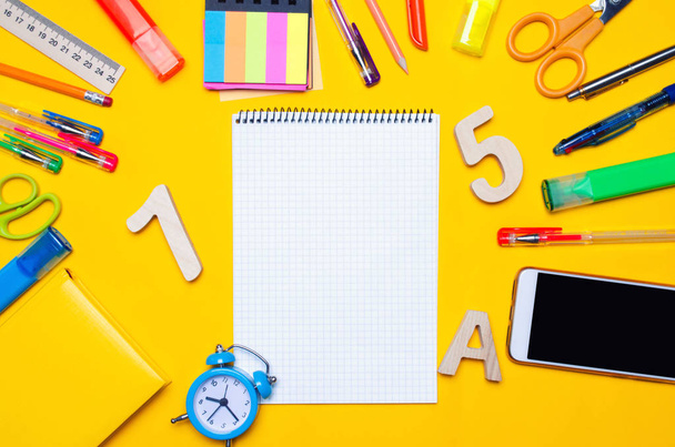 school accessories on a desk on a yellow background. concept of education. stationery. watches, colored pens, phone, markers. notebook. view from above. copy space. top view. flat lay - Photo, Image