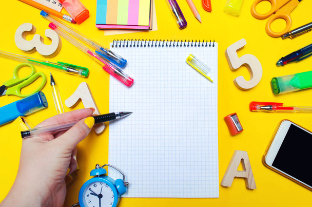 the student makes notes in a notebook. copy space. school accessories on a desk on a yellow background. concept of education. stationery. watches, colored pens, phone, markers. view from above. top view. flat lay. copy space - Zdjęcie, obraz