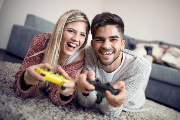 Νεαρό ζευγάρι παίζει βιντεοπαιχνίδια στο σαλόνι - Φωτογραφία, εικόνα