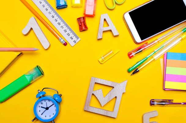 school elections concept. Election check box and school accessories on a desk on a yellow background. education. stationery, watches, colored pens, phone, markers. notebook. view from above. copy space. top view. flat lay - 写真・画像