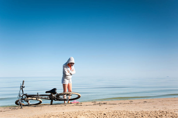 Menina esportiva jovem descansando de andar de bicicleta na costa do mar azul-turquesa. Summertime multicolorido ao ar livre imagem horizontal com fundo céu azul claro
 - Foto, Imagem