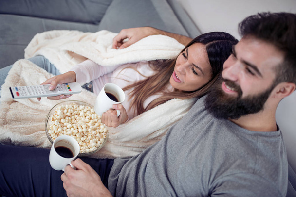 Szczęśliwa para, oglądanie telewizji, picia kawy i jedzenie popcorn na kanapie - Zdjęcie, obraz