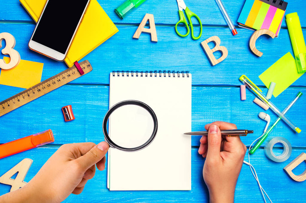 school concept, accessories. the schoolboy points to a notepad. hand with magnifying glass. new ideas, homework solution. back to school. place for text. copyspace - Photo, image