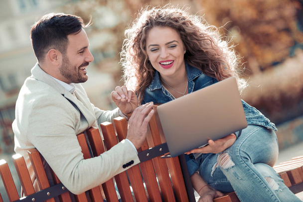 Happy young couple having fun outdoors and smiling, looking on laptop. - Zdjęcie, obraz