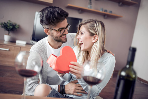 Young couple celebrating at home, man giving girlfriend gift box. - Photo, Image