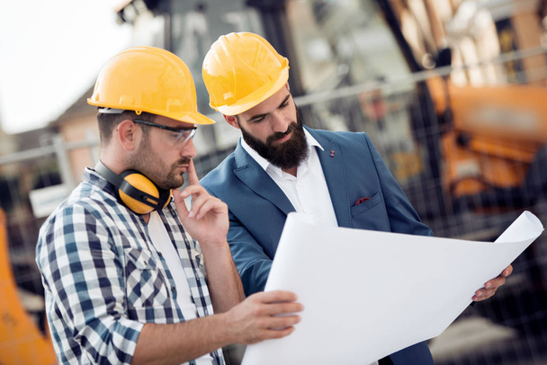 Two engineer builders with blueprint plan at construction site. - Photo, Image