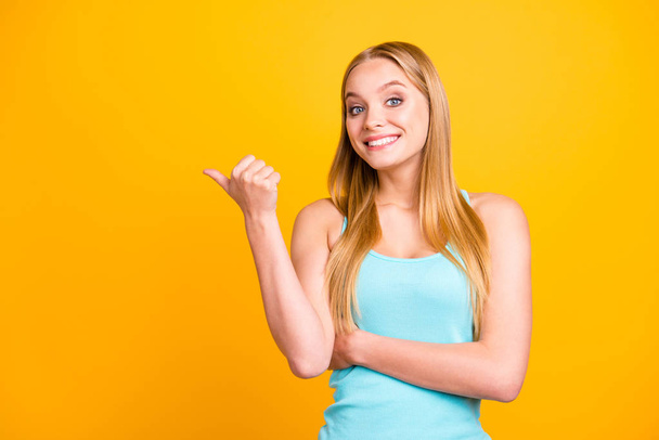 Young and positive girl showing empty place with forefinger looking at camera and make big smile. Female model near copy space for text isolated on yellow background - Valokuva, kuva