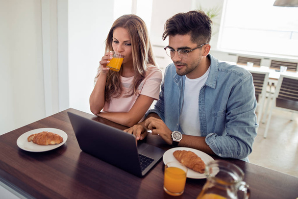 Fiatal aranyos pár reggelizik rövid idő szemöldök-ra laptop. - Fotó, kép
