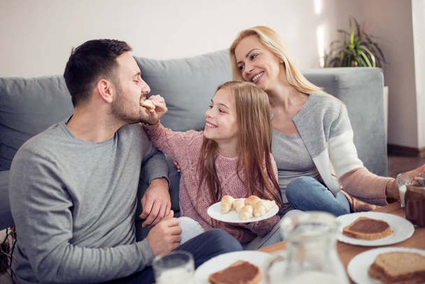 Portrait de jeune famille heureuse prenant le petit déjeuner ensemble à la maison
 - Photo, image