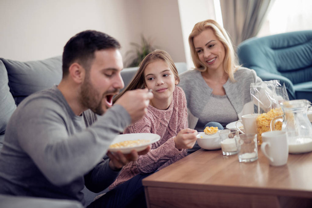 Portrait de jeune famille heureuse prenant le petit déjeuner ensemble à la maison
 - Photo, image