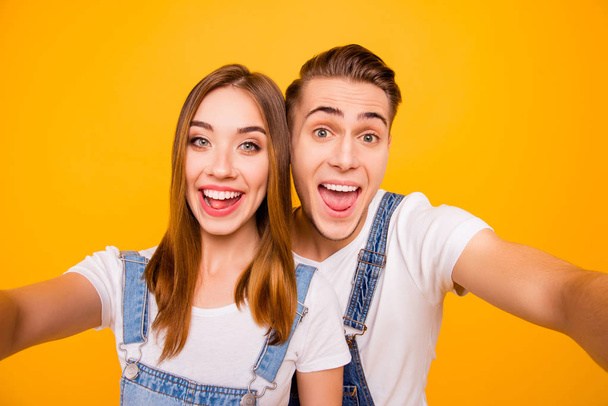 Self portrait of beautiful cheerful funny foolish adorable young cute couple smiling, looking straight with opened mouths over yellow background, isolated - 写真・画像