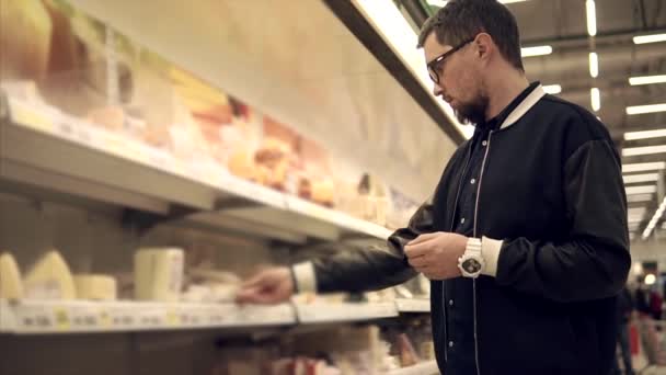 一人の男がスーパーでチーズと肉のパッケージを取ると入れて - 映像、動画