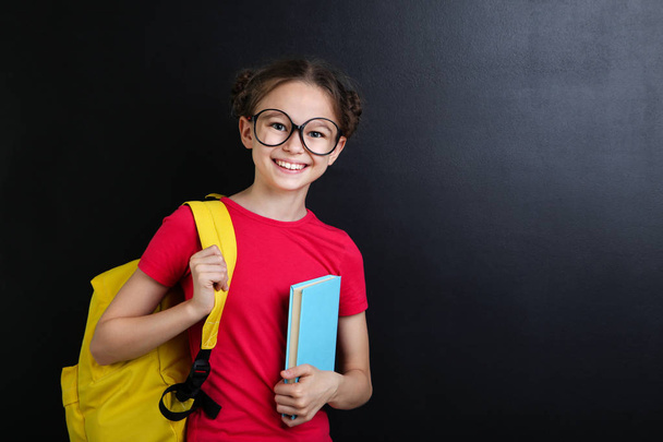 Young girl with backpack and book on blackboard background - Foto, Imagem