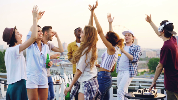 Slow motion of friends dancing with raised hands enjoying music rhythm and laughing while deejay is working with mixing console. Rooftop party, modern lifestyle and youth concept. - Footage, Video