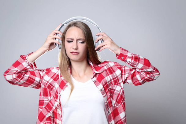 Young woman with headphones on grey background - 写真・画像