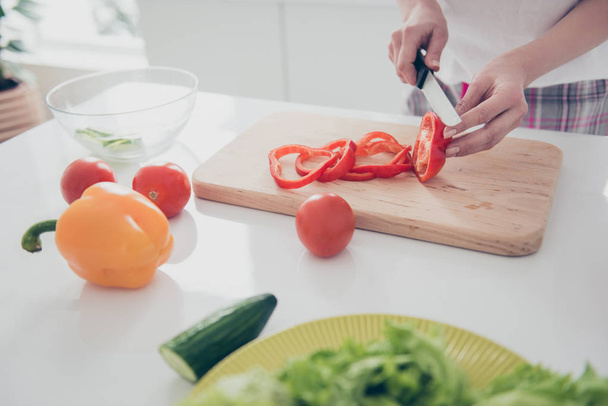 entzückend attraktive schöne, charmante weibliche Hände mit Maniküre Paprika hacken an Bord mit Messer, Kochen schönen Salat. Paprika, Gurken, Tomaten liegen auf weißem Tisch - Foto, Bild