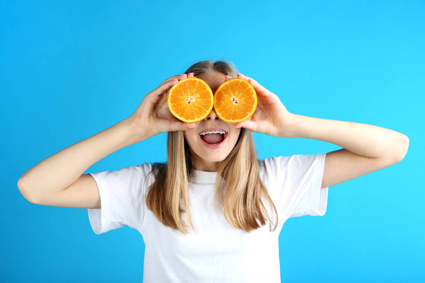 Young smiling girl with orange fruits on blue background - Foto, afbeelding