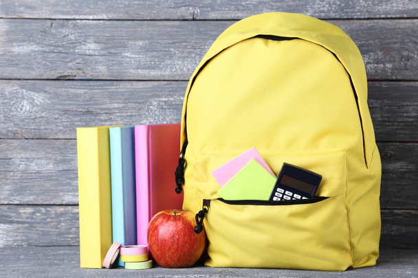 Yellow backpack with school supplies on wooden background - Zdjęcie, obraz