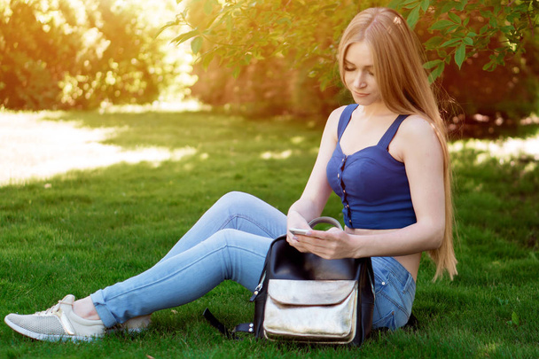 menina sentada no gramado e olhando para o telefone
 - Foto, Imagem