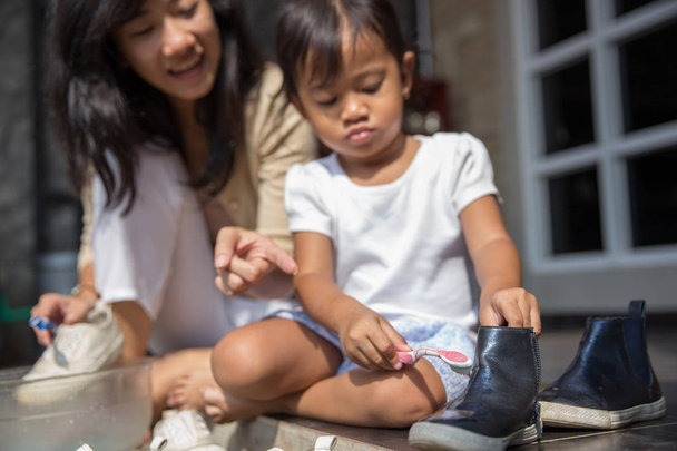 mother with her toddler girl washing their shoes together  - Foto, imagen