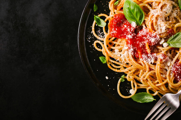 Tasty appetizing classic italian spaghetti pasta with tomato sauce, cheese parmesan and basil on plate on dark table. View from above, top view - Foto, imagen