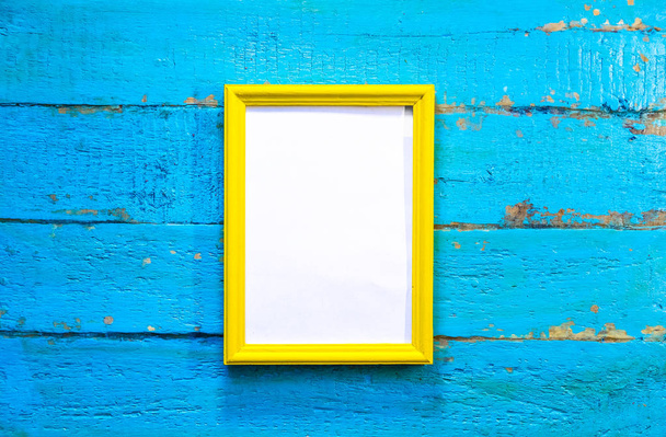 frame for photographs and images of yellow color with a blank white background inside on a blue textured wooden wall - Foto, Bild
