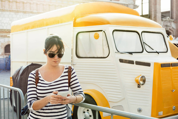 Młoda kobieta nawet pisania wiadomości na jej telefon komórkowy, obok stylu vintage food trucka, na zewnątrz - Zdjęcie, obraz