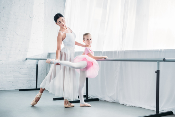 beautiful child in pink tutu practicing ballet with young teacher in ballet studio - Foto, Imagem