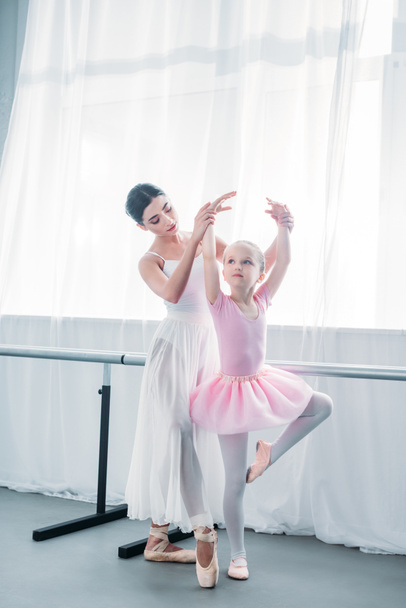 adorable child in pink tutu practicing ballet with young teacher in ballet school   - Foto, afbeelding