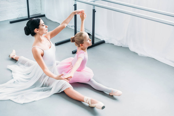 Hochwinkelaufnahme eines entzückenden Kindes in rosa Tutu, das mit einem Lehrer in der Ballettschule übt - Foto, Bild