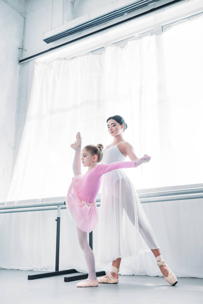 low angle view of young ballet teacher training with child stretching in ballet school - Photo, Image