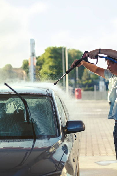 Νεαρός άνδρας τον καθαρισμό του οχήματος με εκτόξευση νερού υψηλής πίεσης. Πλύσιμο αυτοκινήτων detailg - Φωτογραφία, εικόνα
