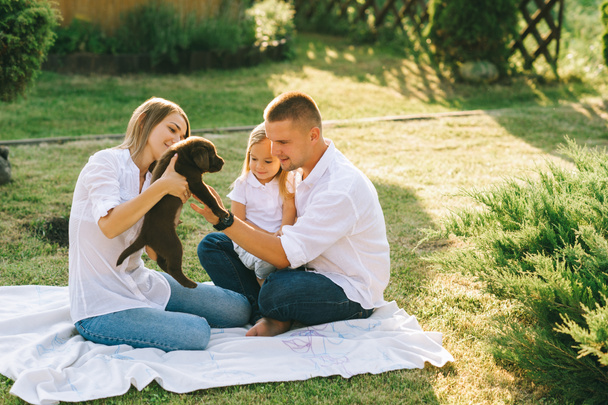 ailesi ile birlikte arka bahçesinde üzerinde dinlenme, küçük kızı ve labrador köpek yavrusu - Fotoğraf, Görsel