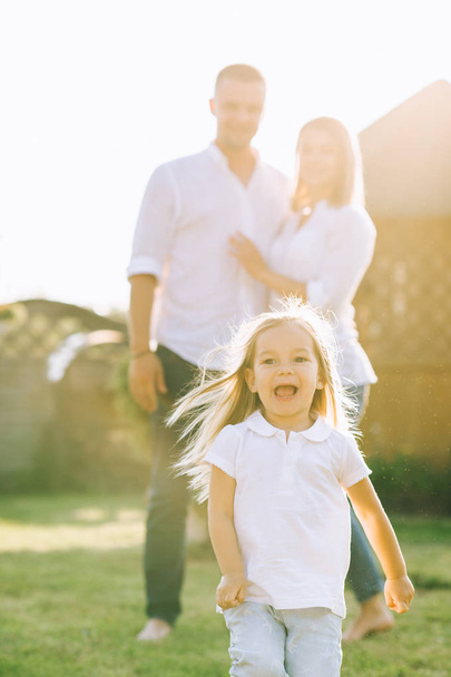 selective focus of little kid running while parents standing behind on backyard - Valokuva, kuva