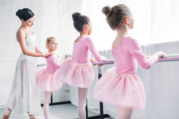 cute little kids in tutu skirts exercising with teacher in ballet school - 写真・画像