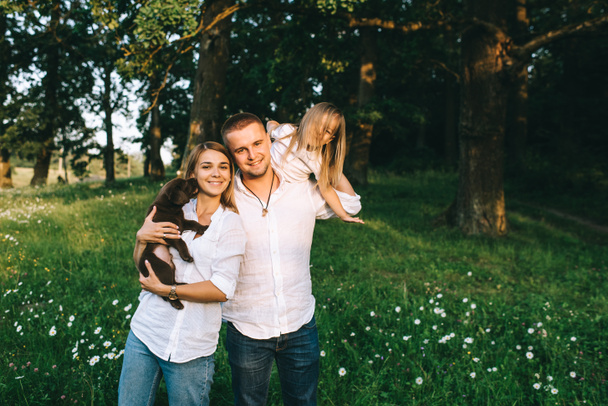 portrait of smiling parents with daughter and little labrador puppy in forest - Foto, immagini