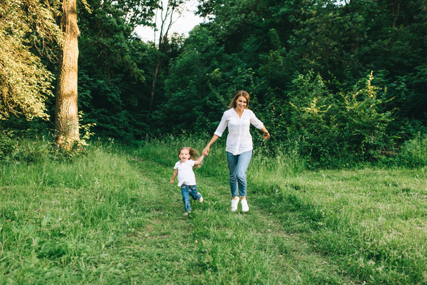 jovem mãe e alegre filha de mãos dadas enquanto correm juntos na floresta
 - Foto, Imagem
