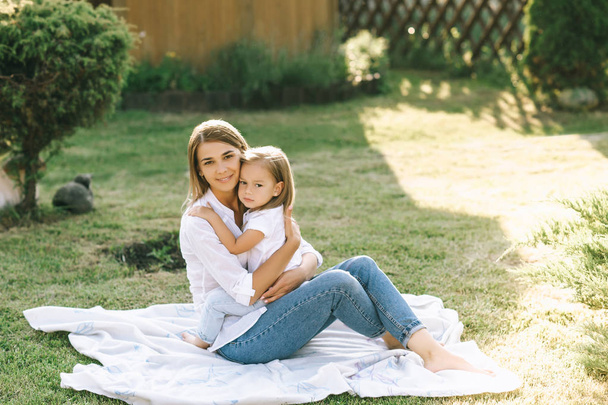 щаслива мати і маленька дочка обіймають один одного, відпочиваючи разом на тканині на задньому дворі
 - Фото, зображення