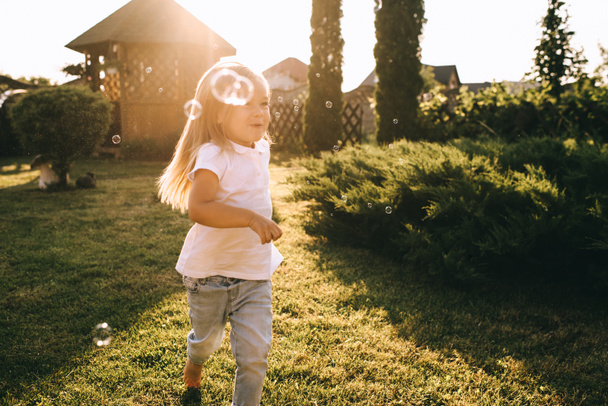 μικρό παιδί διασκεδάζοντας με σαπουνόφουσκες στην πίσω αυλή - Φωτογραφία, εικόνα