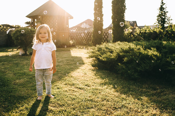 cute little blond child looking at camera while standing on backyard - Photo, Image