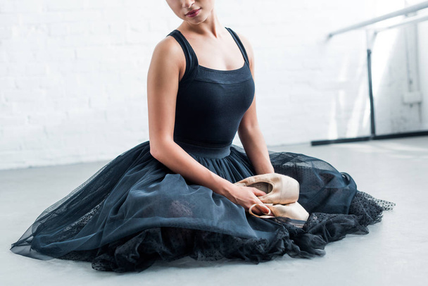 Schnappschuss der schönen jungen Ballerina, die sitzt und Spitzenschuhe hält - Foto, Bild