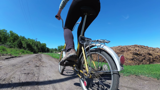 村の田舎の道に沿ってヴィンテージ自転車に乗る若い女性。スローモーション. - 映像、動画