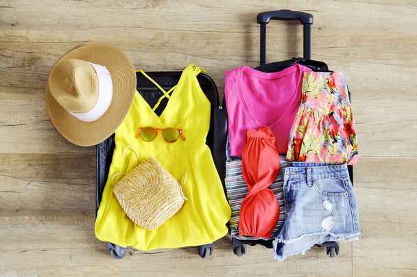 Open suitcase fully packed with folded women's clothing and accessories on the floor. Woman packing for tropical vacation concept. Female luggage w/ things. Background, close up, copy space, top view. - Photo, Image