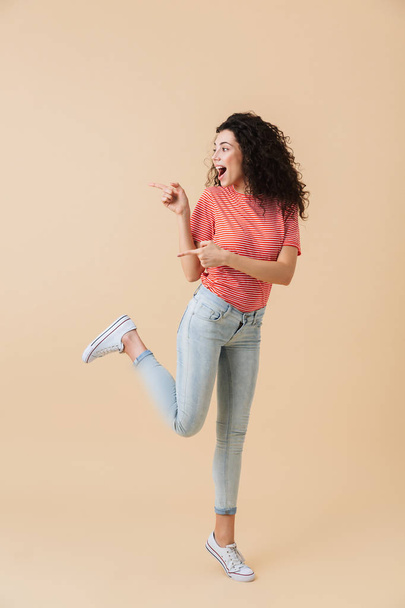Photo of excited emotional young woman isolated over beige wall background showing copyspace. - Photo, image