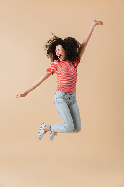 Image of pretty young woman jumping isolated over beige wall background. - Фото, изображение