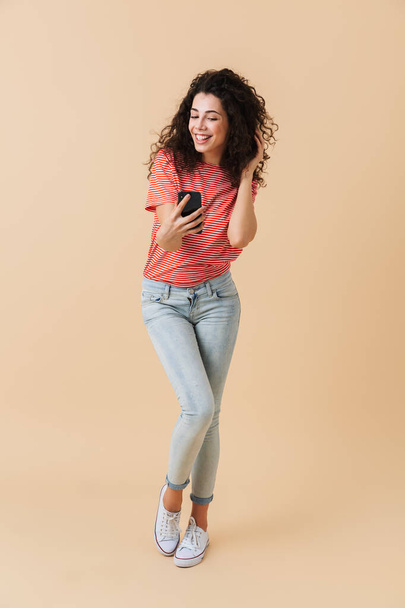 Full length portrait of a happy casual girl taking a selfie with mobile phone isolated over beige background - Photo, Image