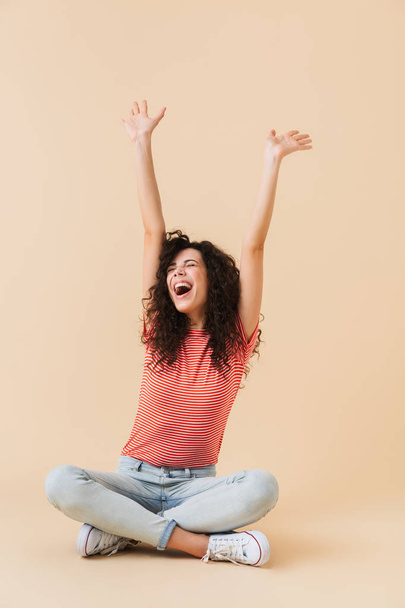 Photo of screaming happy young woman sitting isolated over beige wall background. - Fotografie, Obrázek