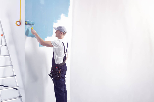 Decorator wearing overalls painting a room blue. Place your graphic on the empty wall - Fotó, kép