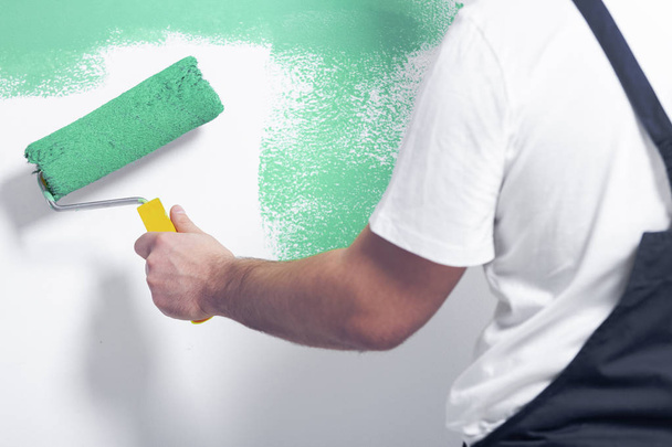 Close-up of worker with roller painting white wall on green - Foto, afbeelding